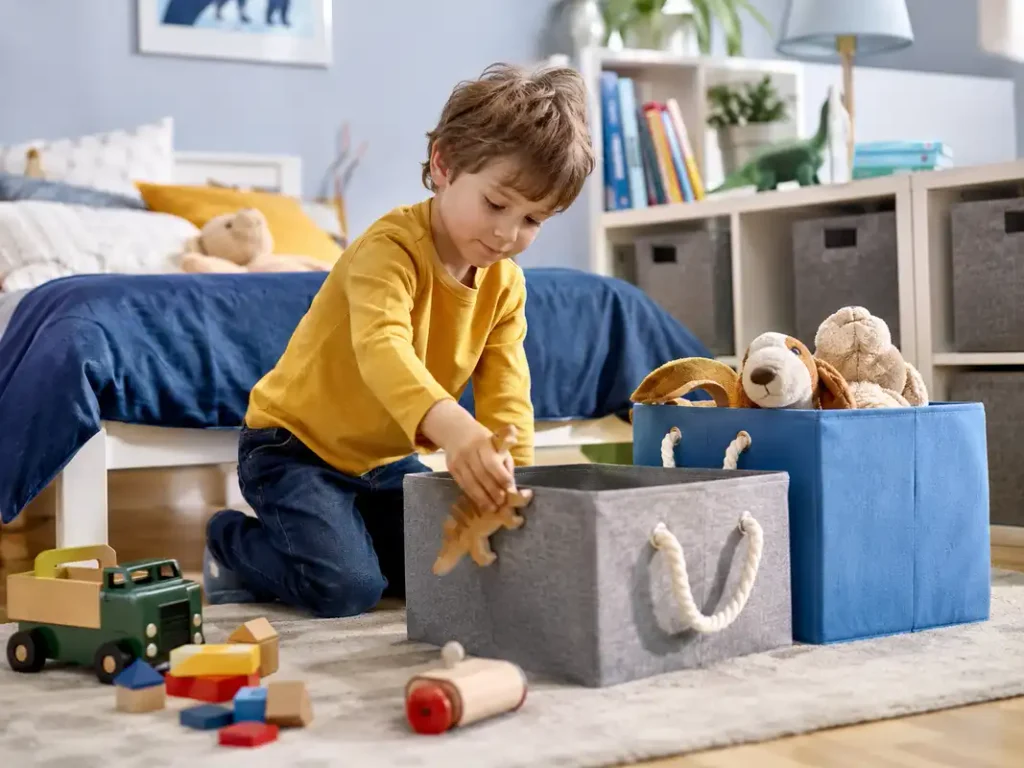 Kind räumt sein Kinderzimmer auf und sortiert Spielzeug in Aufbewahrungsboxen